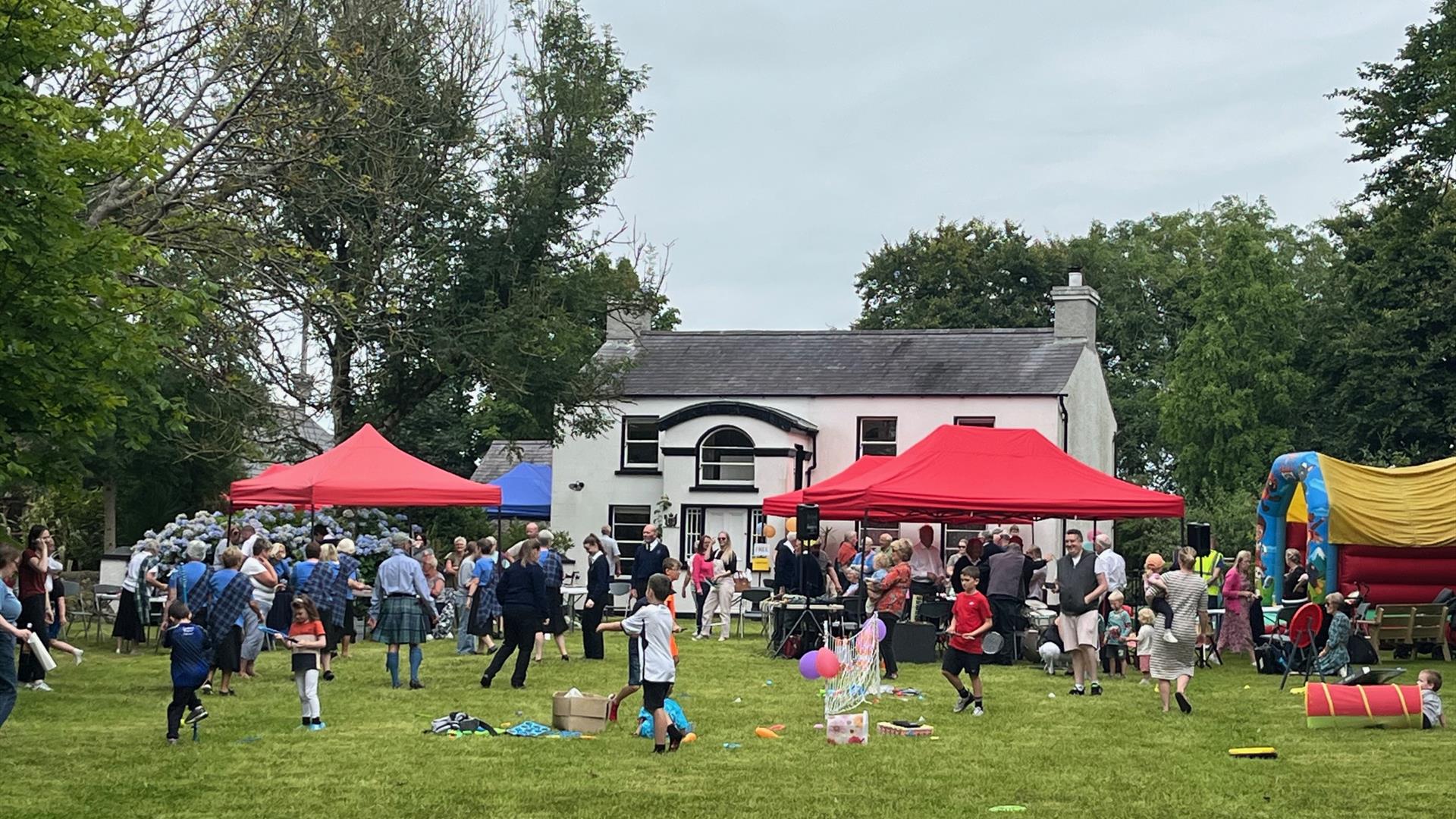 Image shows lots of people enjoy themselves outside of The Ballance House, there is a bouncy castle, lawn games and gazebo's.