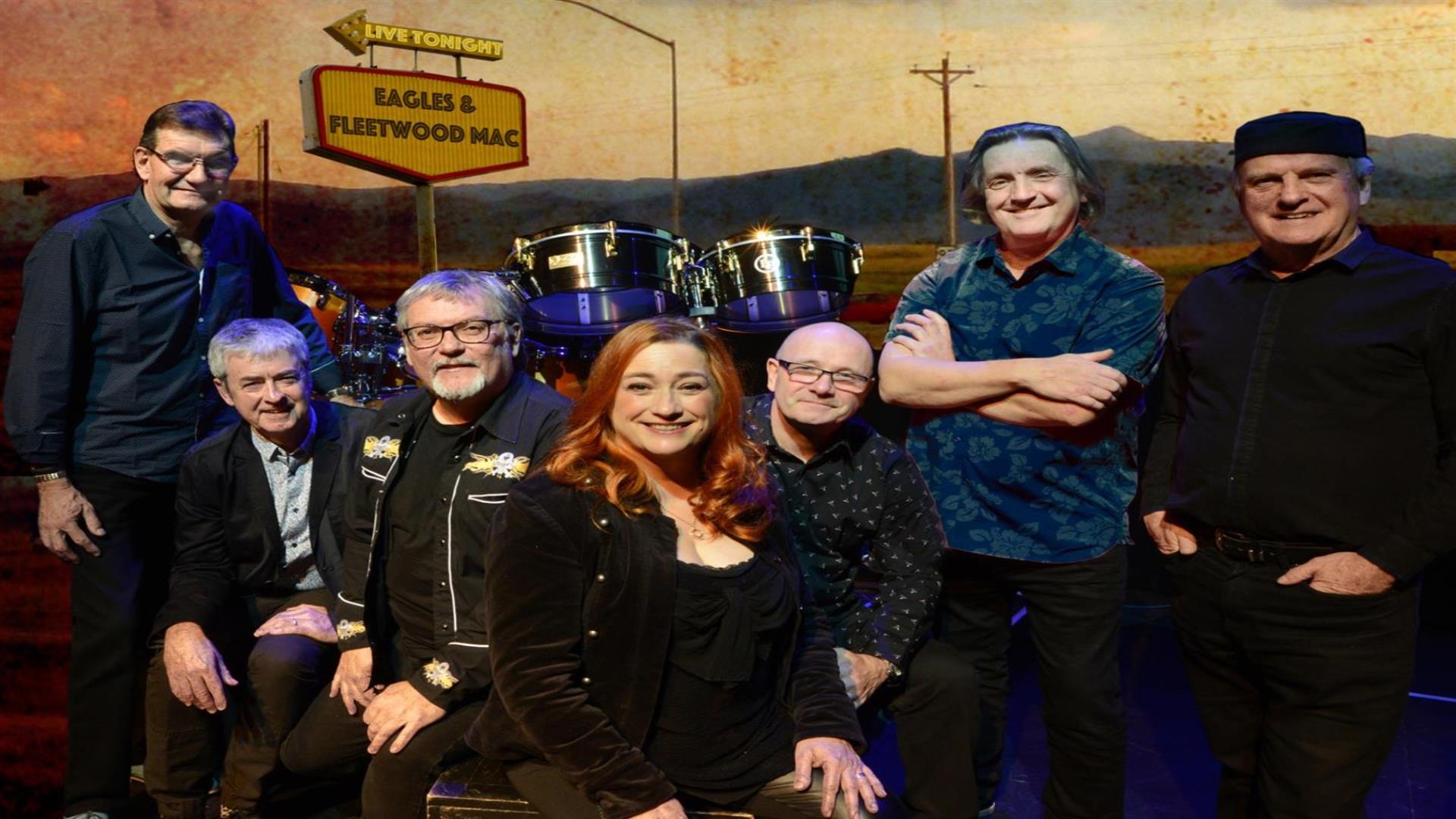 Image shows The Illegals bandmates with drum set and Eagles and Fleetwood Mac sign in background.