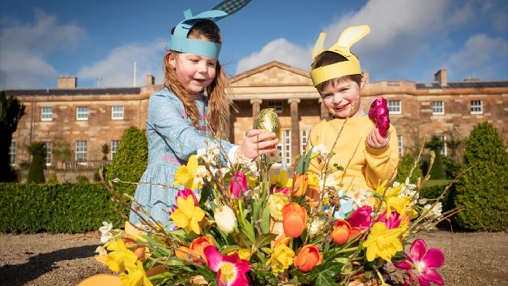 Image is of children holding Easter eggs in a basket in front of Hillsborough Castle