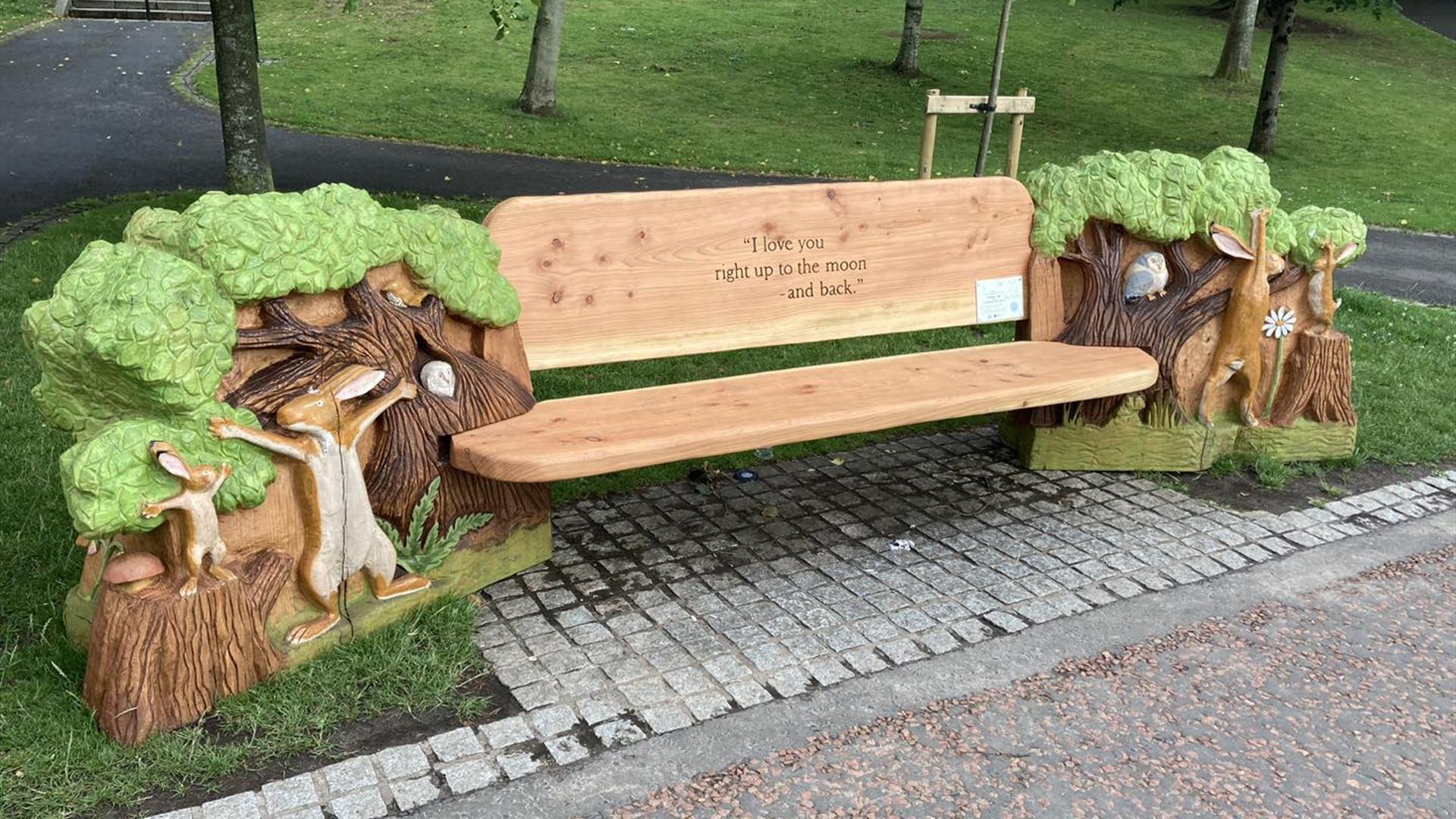 Image shows wooden bench in a park with engraving 'I Love you to the moon and back7