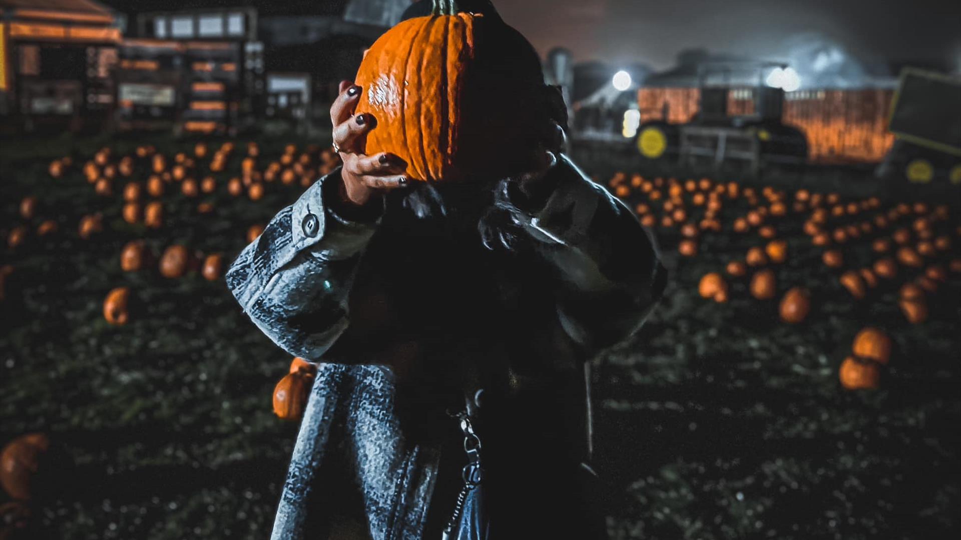 Woman holding up pumpkin in dark pumpkin patch at Streamvale Farm
