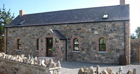 Image shows front of stone cottage with gravel driveway