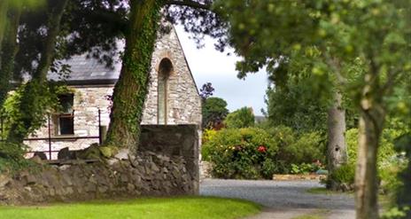 Image shows entrance to property surrounded by trees and bushes.