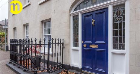 Image shows royal blue front door with iron railing to the left of the door Door leads out onto footpath on street