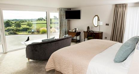 Shows image of double bedroom with large window looking out at countryside view