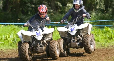 Image is of 2 children on mini quad bikes