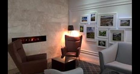 Image shows lounge area with chairs and various paintings on the wall