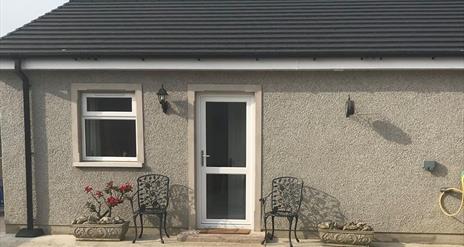 Image is of front of the property with wrought iron chairs at either side of the front door