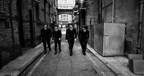 Black and White Image shows Beatles Tribute members in a alleyway dressed in suits.