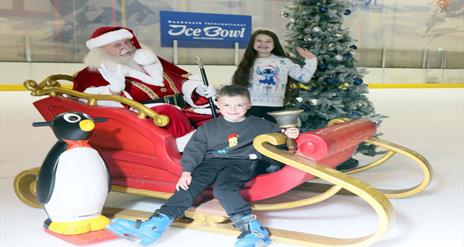 Santa Claus on a sleigh on the ice rink with two children at Dundonald International Ice Bowl