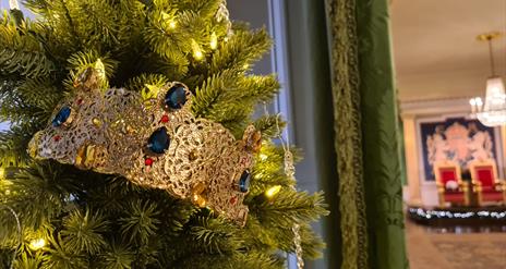 An image of a Christmas tree by the entrance to the Throne Room. The tree has lights and a gold crown with jewels.