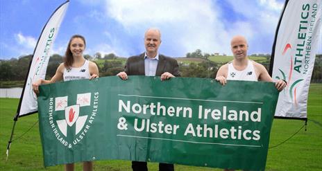 Image is of two runners holding a banner advertising Northern Ireland & Ulster Athletics