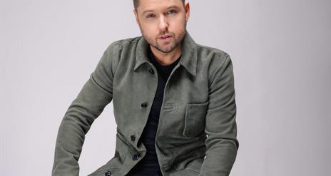 Image shows Derek Ryan sitting on stool.