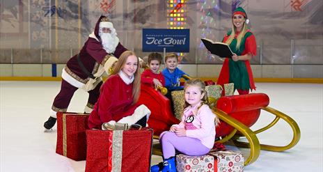 Santa & Elf on the rink with children on sleigh and sitting on Christmas presents