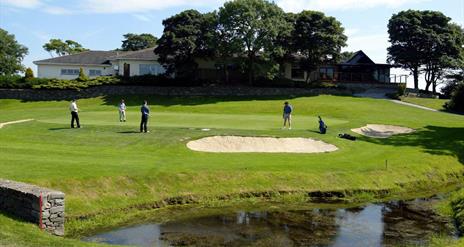 Image is of golf course with golfers playing and lake in the foreground