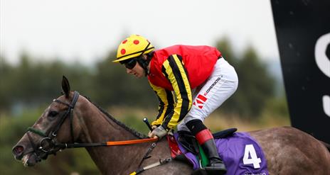 Jocket wearing red top riding horse