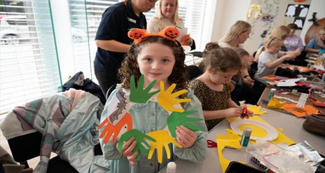 Image shows children's workshop and girl holding up workshop wreath display