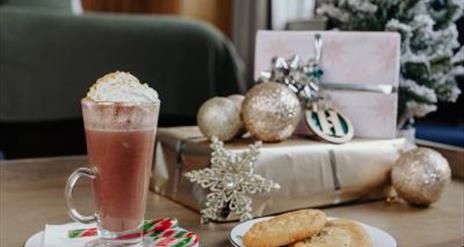 Image shows room in Haslem Hotel with dark green colours with silver wrapped presents and an image of a Christmas latte with peppermint stick and a pl