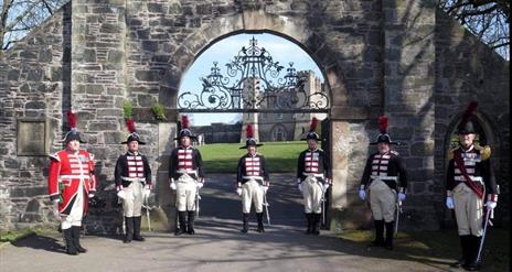 Image shows 7 guards in traditional dress outside the gates of Hillsborough Fort.