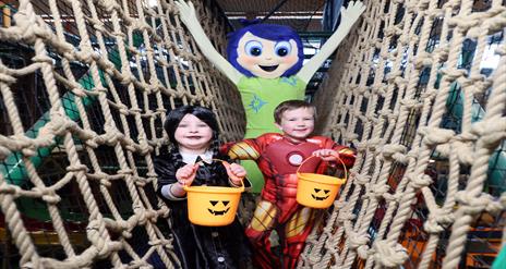 Image shows two children in halloween costume holding pumpkin buckets with a character behind them and all standing on the nets at Indiana Land