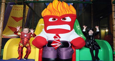 Image shows yellow and green sides at Indiana land with character positioned in the middle and two children sitting on each of the slides dressed in H