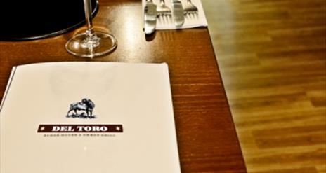 Images shows table laid with cutlery and wine glass with Del Toro restaurant menu also on table