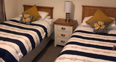 Image shows twin bedroom with bedside table and lamp between the beds
