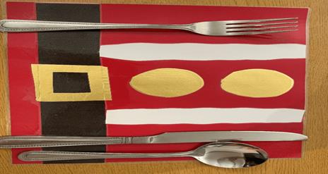 Image is of a festive place mat with cutlery