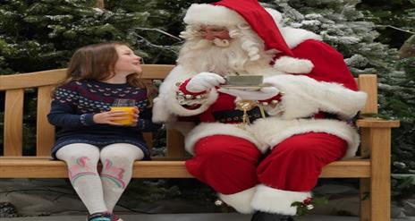 Image is of Santa on a bench with a little girl