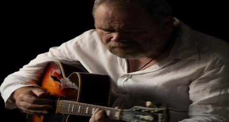 Image is of musician Ken Haddock playing acoustic guitar
