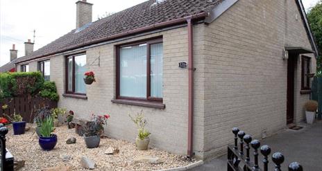 An Image of the front of the semi-detached bungalow with driveway to the side and set of gates.