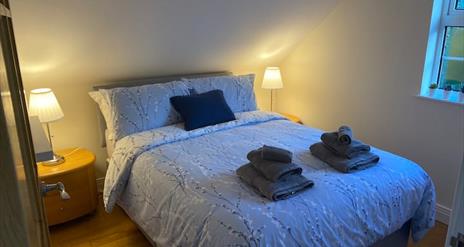 Image shows double bedroom with beside tables and lamps and wooden floor