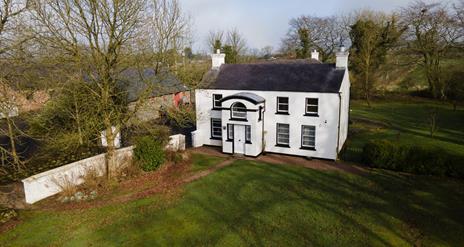 Image is of the front of Ballance House with lawn and fields around it