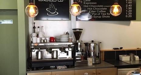 Image shows front counter of Coffee Inc premises with barista machines and traybakes and scones in covered display.