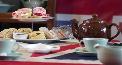 Image shows a tea set with cakes and sandwiches.