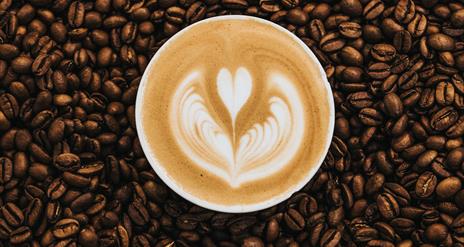 Image shows coffee beans and cup of coffee sitting in the middle.