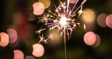 Hand holding a sparkle up against Christmas lights