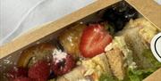 Picnic box of treats including raspberries, traybakes, iced cupcakes, sandwiches, strawberries, a little salad
