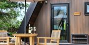 Private outdoor seating area at a luxury A-frame lodge, with a parasol, table, chairs and prosecco set beside the lodge entrance.