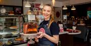 Image shows smiling member of staff holding a large  chocolate and orange cake
