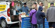 Image shows a man selling fish from his van whilst customers queue up