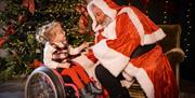 Santa and a little girl in a wheel chair in front of a Christmas tree