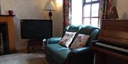 Image is of lounge area with leather sofa, piano and TV