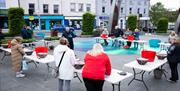 Image shows tables with hanging baskets and members of the public listening to one of the gardeners on how best to design them.