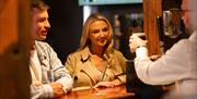 Image is 2 customers waiting on a pint of Guinness being poured