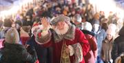 Santa waving at camera with crowd behind him