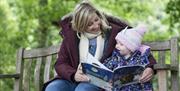 A mother and child sitting together on a garden bench reading The Gruffalo's Child.