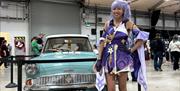 Image is of female dressed up for Comic Con standing beside an old car