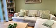 Image shows living room with sofa, bookcase, coffee table and wooden flooring