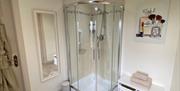 Image shows bathroom with shower, mirror and bath robe hanging on back of door